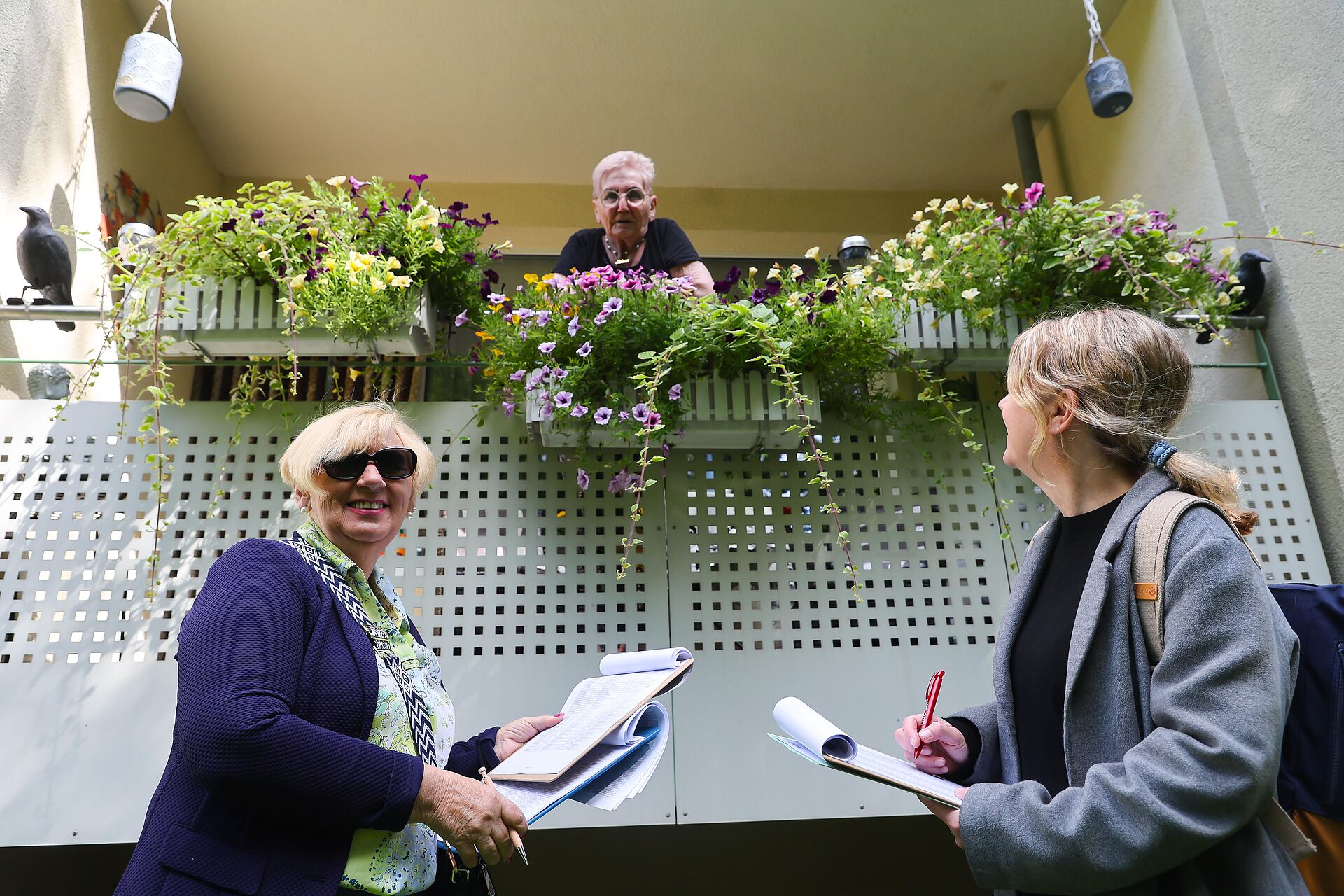 Zwei Jury-Mitglieder sprechen mit einer Mieterin, die ihren Balkon wundervoll bepflanzt hat